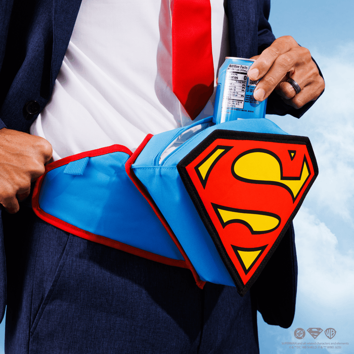 A close-up of a person in a navy suit, white shirt, and red tie holding a blue beverage can into a Superman-themed cooler belt. The cooler belt is bright blue with red trim and a large red-and-yellow Superman shield emblem on the front.