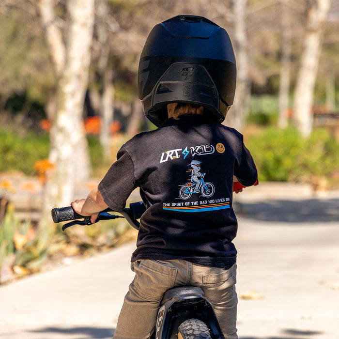 A young boy wearing the LRT x SUPER73 Limited Edition Collab Tee sitting on a SUPER73-K1D ebike and facing away from the camera.
