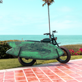 A SUPER73-S2 Laguna sits parked on a grassy area near the beach. A MBB Dual Sport Surf Rack is installed on the bike and a green and black marbled surfboard sits within the rack.